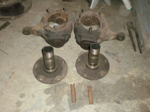 1995 Ford Bronco - Two used front wheel hubs and steering knuckles are laid out on a concrete surface, with two small metal rods nearby.
