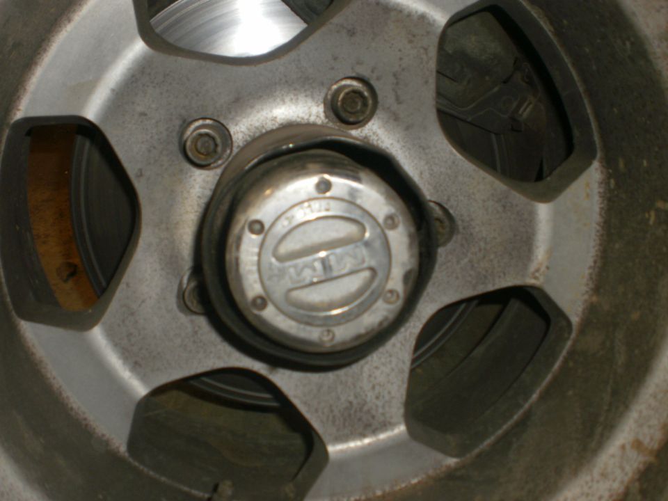 Close-up of a metal wheel hubcap with "4x4" text. The wheel has five spokes and a brake rotor is visible