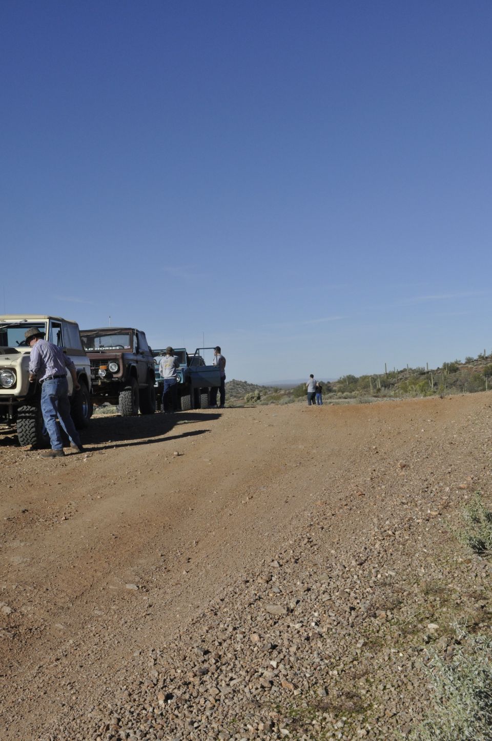 Several off-road vehicles parked on a dirt road in a desert landscape
