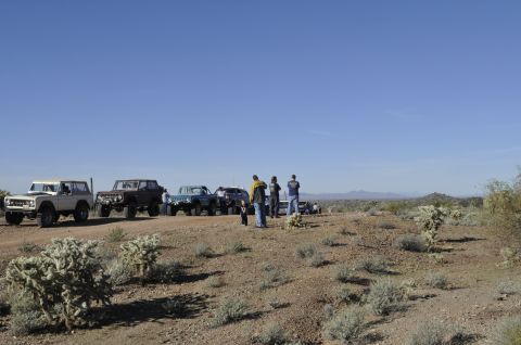 1991 Ford Bronco - A convoy of off-road vehicles is gathered in a desert environment under a clear blue sky.