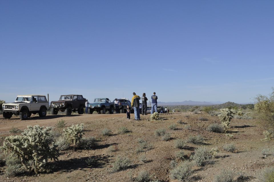 Several off-road vehicles parked on a dirt road in a desert landscape with people standing around