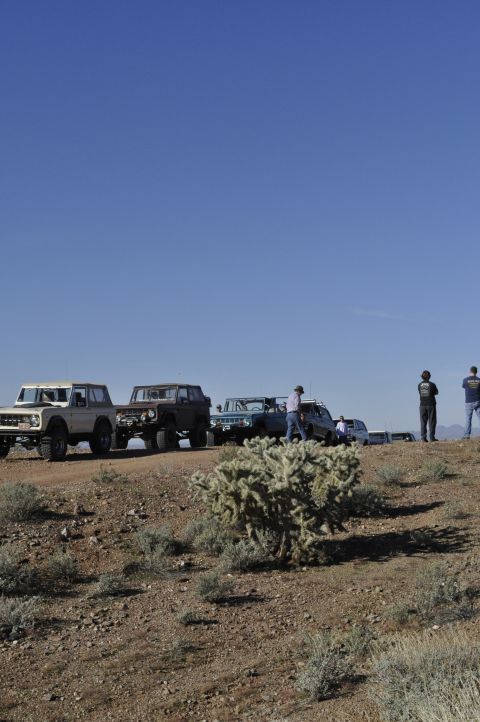 1991 Ford Bronco - Several vehicles, including a tan 1978 Ford Bronco, are parked on a dusty road under a clear blue sky.