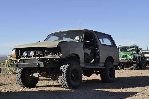 1991 Ford Bronco - A modified Ford Bronco is parked in a line with other off-road vehicles under a clear blue sky.