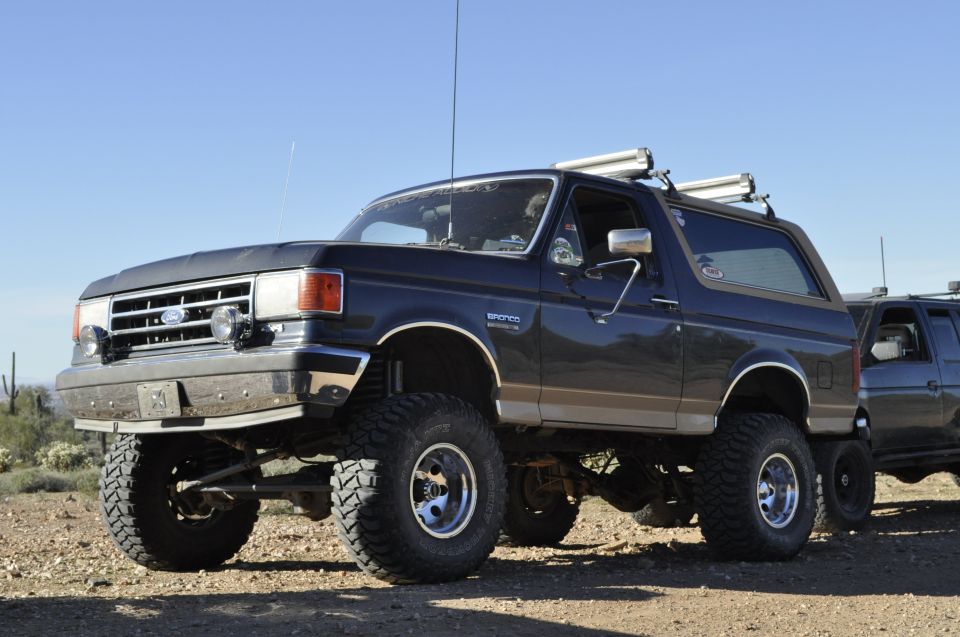 Dark blue Ford Bronco with lifted suspension and off-road tires, seen from a 3/4 front angle