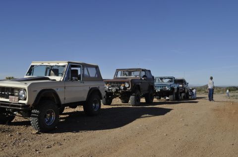1991 Ford Bronco - A convoy of Ford Broncos is lined up on a dusty track under a bright, cloudless sky.