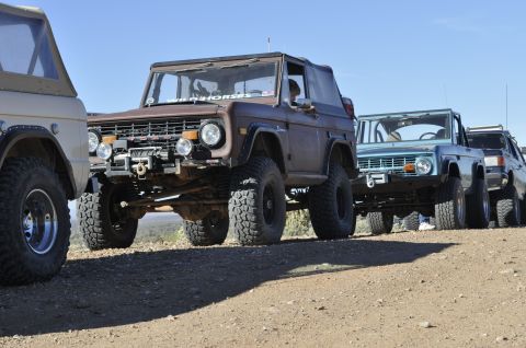 1991 Ford Bronco - A line of Ford Broncos are parked on a dusty trail under a clear blue sky.