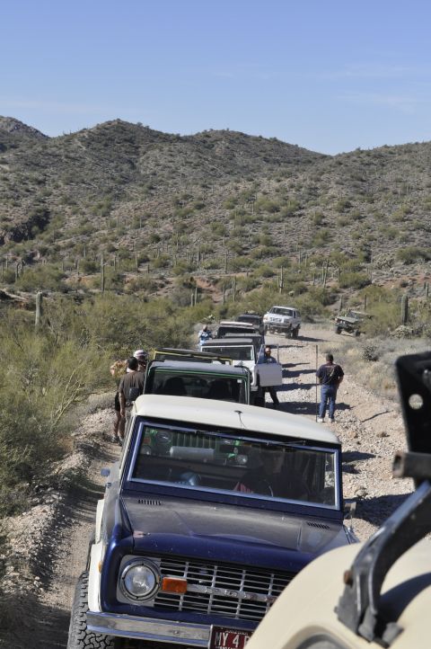 1991 Ford Bronco - A line of off-road vehicles navigates a desert trail, with a classic Ford Bronco leading the pack.