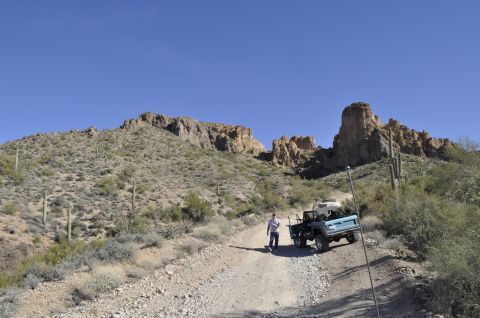 1991 Ford Bronco - Two off-road vehicles navigate a dusty desert trail with mountains in the background.