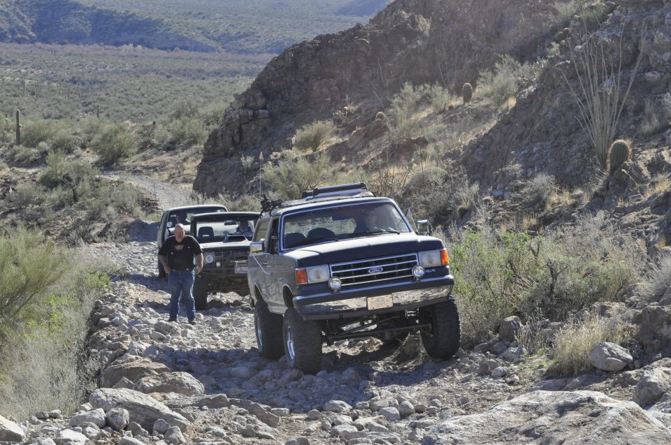 1991 Ford Bronco driving on a rocky desert trail with two other vehicles behind it