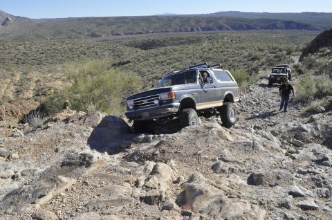 1991 Ford Bronco - A lifted Ford Bronco navigates a challenging rocky terrain in a desert landscape.