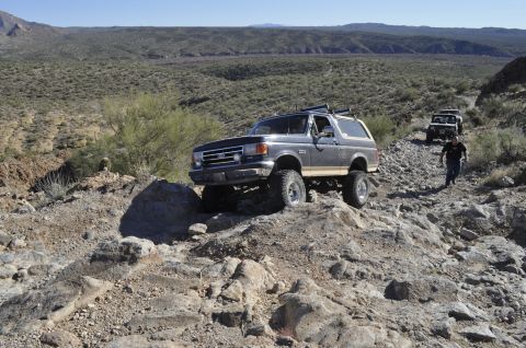 1991 Ford Bronco - A gray Ford Bronco navigates a rocky off-road trail with other vehicles following behind.