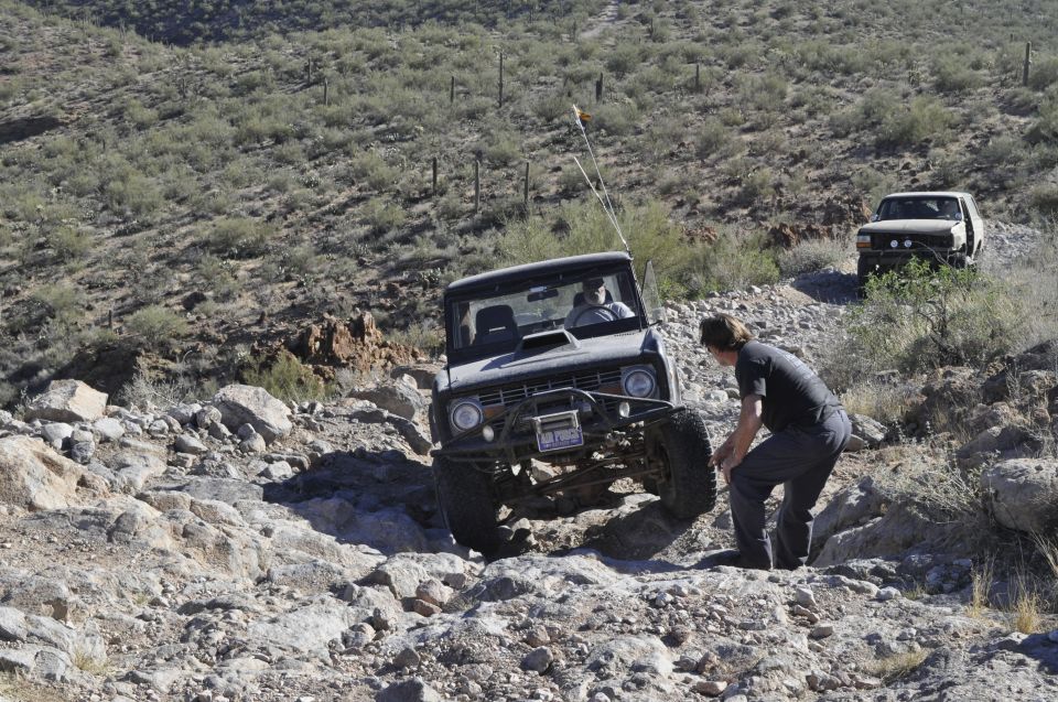 Modified Ford Bronco off-roading with another vehicle behind it on a rocky hill