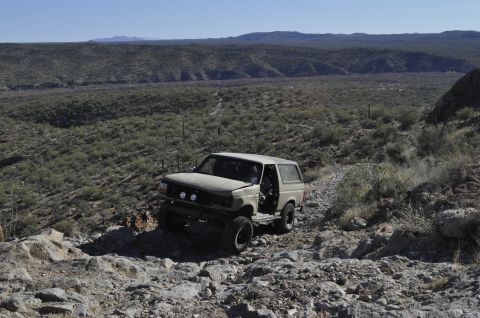 1991 Ford Bronco - A tan Ford Bronco navigates a rocky, off-road trail in a desert landscape.