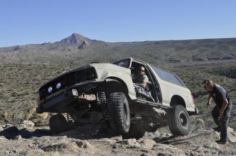 1991 Ford Bronco - This 1991 Ford Bronco is captured mid-off-road adventure, with its doors open and tires gripping the , rocky landscape.