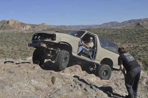 1991 Ford Bronco - Off-road Bronco navigating a challenging rocky trail under a clear blue sky.