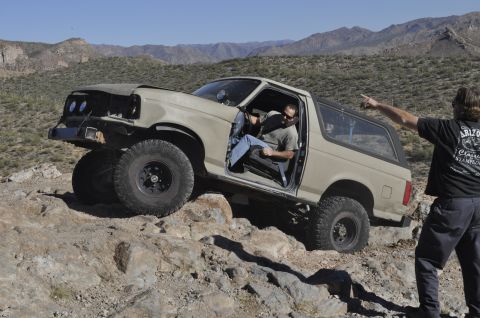 1991 Ford Bronco - A man in a tan Ford Bronco navigates a rocky desert trail while another man points.