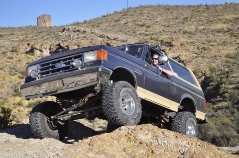 1991 Ford Bronco - This lifted Ford Bronco navigates a desert trail with a large rock formation in the background.