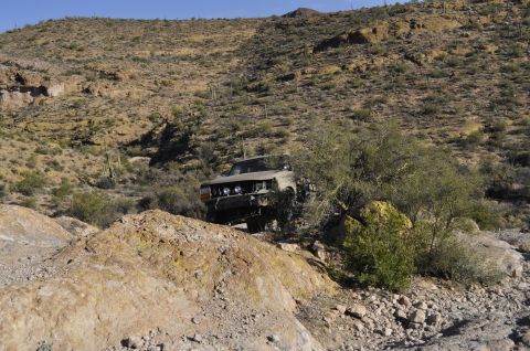 1991 Ford Bronco - A tan off-road vehicle navigates a rocky, desert landscape with sparse vegetation and cacti.