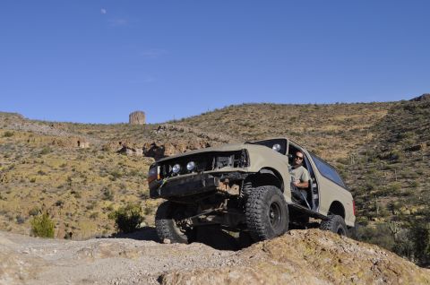 1991 Ford Bronco - A tan 1991 Ford Bronco navigates a rocky, desert terrain with a clear blue sky overhead.