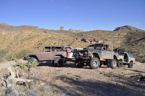 1991 Ford Bronco - Modified Ford Broncos are parked in a desert area with mountains in the background.
