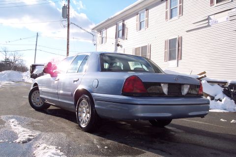 2001 Ford Crown Victoria - A blue 2001 Ford Crown Victoria sedan is parked outside a white building on a sunny day with snow on the ground.