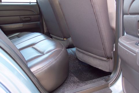 2001 Ford Crown Victoria - The rear interior of a police vehicle, dark leather seats and durable black floor matting, suggests a functional and utilitarian design.