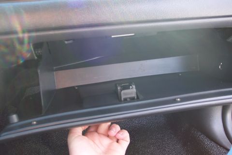 2001 Ford Crown Victoria - The interior of a vehicle shows an open, empty glove compartment with a hand reaching to close it.