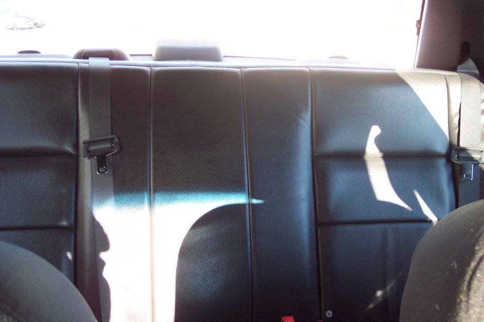 Black leather rear car seat with visible seat belts and headrests