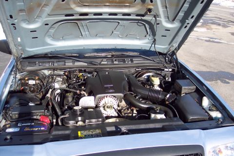 2001 Ford Crown Victoria - The engine compartment of a light blue vehicle is open, revealing the engine, battery, and various engine components.