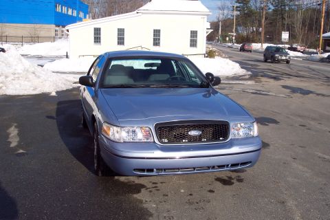 2001 Ford Crown Victoria - A blue sedan is parked on a street with snow on the ground. The front of the car is visible.