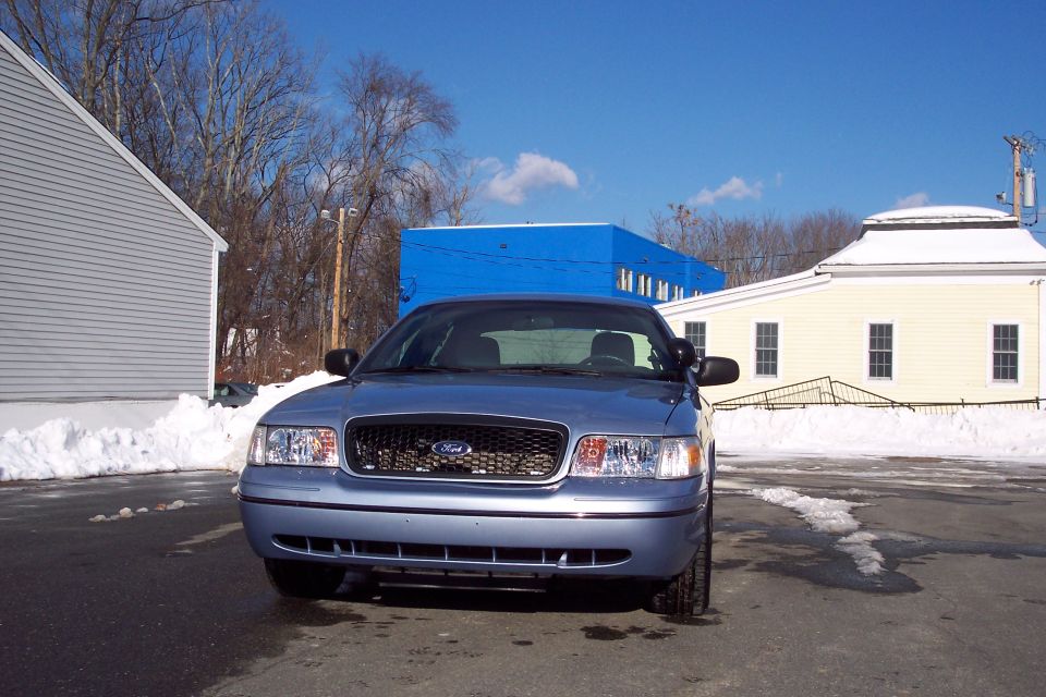 Blue 2001 Ford Crown Victoria parked in front of buildings with snow on the ground