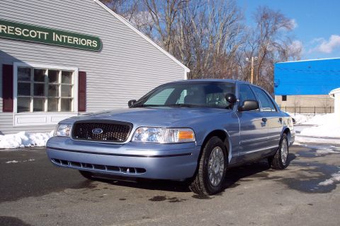 2001 Ford Crown Victoria - A blue 2001 Ford Crown Victoria sedan is parked in front of a building on a sunny day.