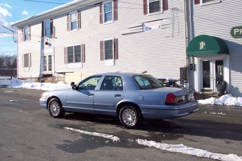 2001 Ford Crown Victoria - A light blue 2001 Ford Crown Victoria sedan is parked in front of a building with snow on the ground.