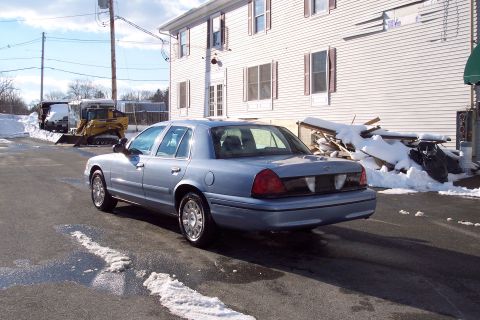 2001 Ford Crown Victoria - A light blue 2001 Ford Crown Victoria is parked in a lot with snow and construction equipment in the background.