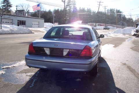 2001 Ford Crown Victoria - The rear of a blue Ford Crown Victoria is visible, with a building and an American flag in the background.