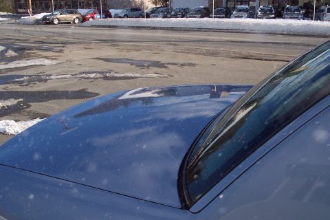2001 Ford Crown Victoria - A blue sedan's hood and windshield are in focus, with a snowy parking lot and other vehicles in the background.