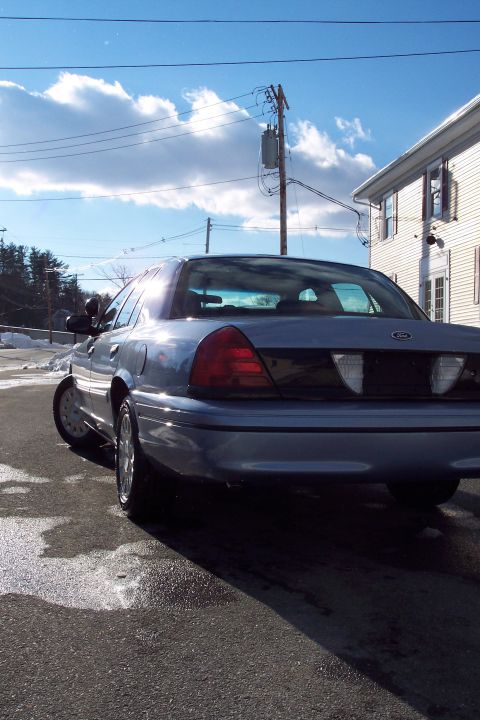 2001 Ford Crown Victoria - Rear view of a blue 2001 Ford Crown Victoria parked on a wet road under a cloudy sky.