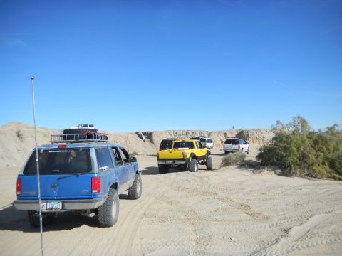 1997 Ford Ranger - Several off-road vehicles are driving through a sandy, desert landscape under a clear blue sky.