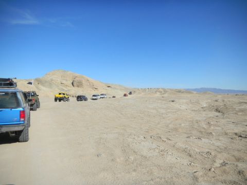 1997 Ford Ranger - Several off-road vehicles drive through a sandy desert terrain under a clear blue sky.