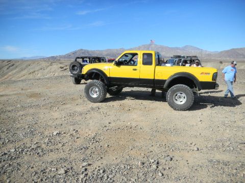 1997 Ford Ranger - A lifted yellow pickup truck is parked in a desert area with another off-road vehicle visible behind it.