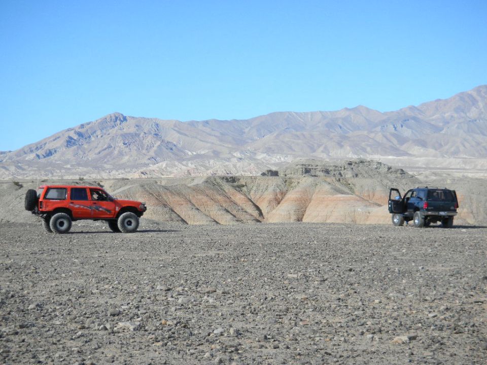 Two SUVs parked in a rocky desert with mountains in the background