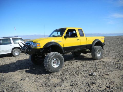 1997 Ford Ranger - A yellow Ford Ranger pickup truck with off-road modifications is parked in a dry, dusty landscape.