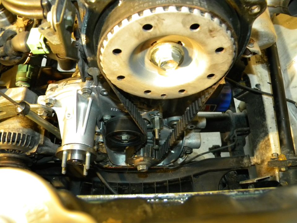 Engine front with timing belt cover removed showing cam sprocket, belt, tensioner and water pump