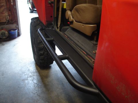 1989 Ford Bronco - Side view of a red SUV with a black running board and a large off-road tire.