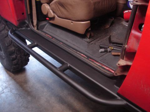 1989 Ford Bronco - Close-up view of the interior of a red vehicle, highlighting a black rock slider and a brown seat, with tools visible on the floor.