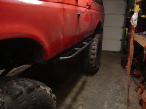 1989 Ford Bronco - Side profile of a red 1989 Ford Bronco with custom rock sliders and aggressive tires.