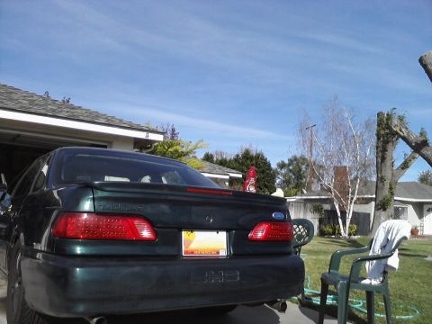 1995 Ford Taurus - The rear of a dark green 1995 Ford Taurus is visible in a driveway on a sunny day.