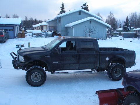 2001 Ford F-350 - Side view of a black 2001 Ford F-350 pickup truck modified with a lift kit and aftermarket bumper, parked in a snowy residential area.