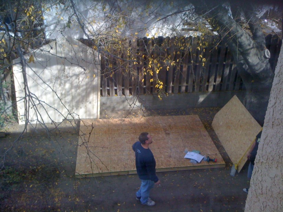 Two men working on a construction project in a backyard with plywood sheets on the ground