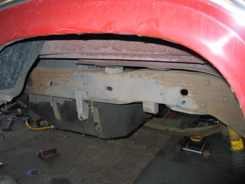 1984 Ford Bronco - The undercarriage of a red vehicle shows a rusty frame and fuel tank, with tools scattered on the floor.